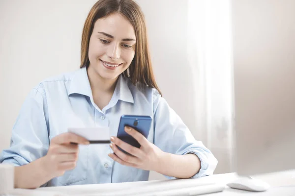 Online payment. Smiling girl using mobile phone pays by credit card.