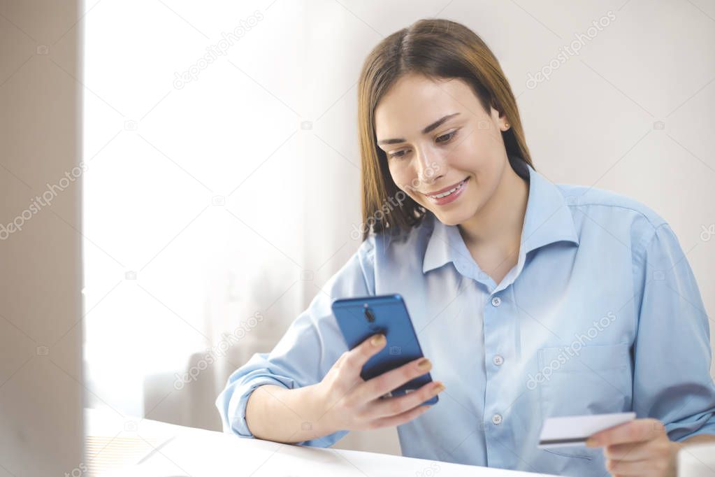 Online payment. Smiling girl using mobile phone pays by credit card.  