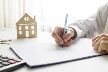 Bir emlakçı masasında otururken bir belge hazırlıyor..