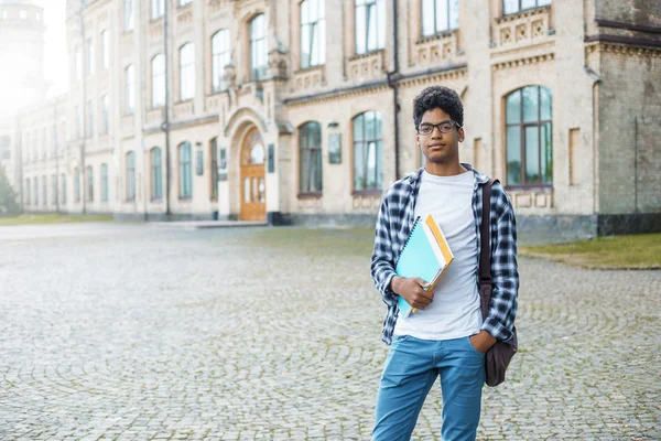 Genç bir Afro-Amerikan öğrenci siyah adam üniversite arka plan portresi. Gülümseyen genç erkek karışık ırk üniversite yakınında duran kitap tutar.