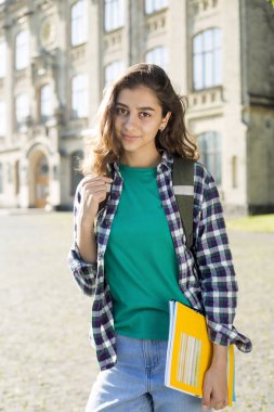 Gülümseyen Hintli genç kız öğrenci üniversitenin arka planında duran eğitim kitapları tutar. Üniversiteye yakın mutlu esmer kız. 