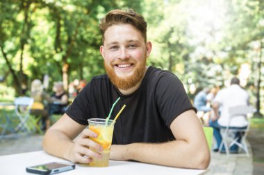 Gülümseyen şık kızıl saçlı sakallı genç adam kafede hafif bir içki içiyor..