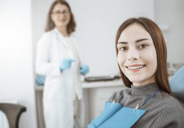 Genç bir kadın bir diş sandalyesinde oturur ve beyaz ve sağlıklı dişler ile gülümsüyor. Doktor ve mutlu hasta. 
