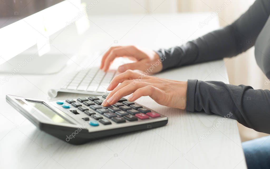 Hand of an accountant counts on a calculator and writes a financial report.