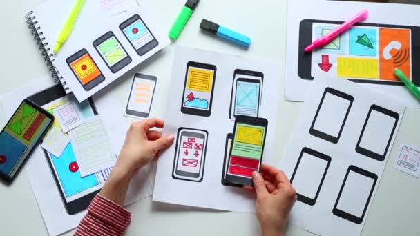 Webデザイナーは 携帯電話アプリケーションへのインターフェイスに取り組んでいます 開発者は スマートフォンのユーザーアプリケーションのスケッチを描きます — ストック動画