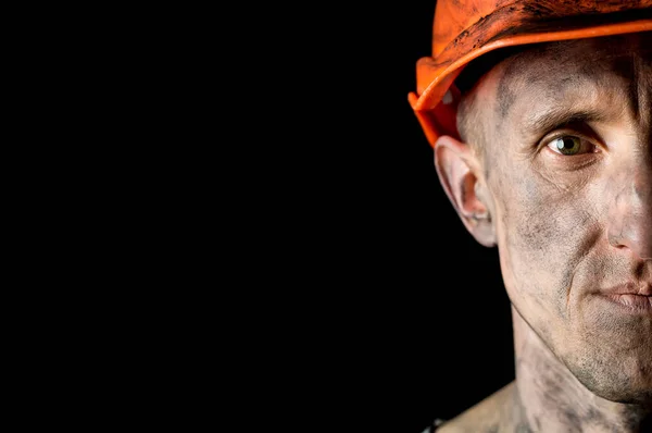 The face of a male miner in a helmet on a black background. Copy space.