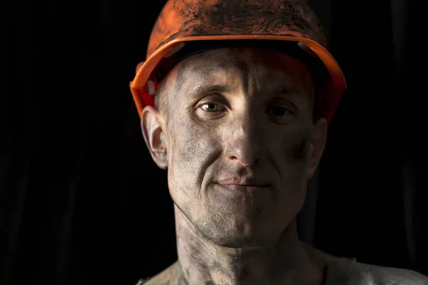 The face of a male miner in a helmet on a black background.