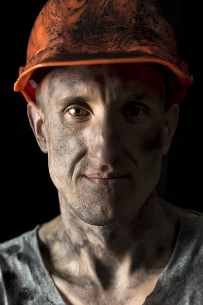 The face of a male miner in a helmet on a black background.