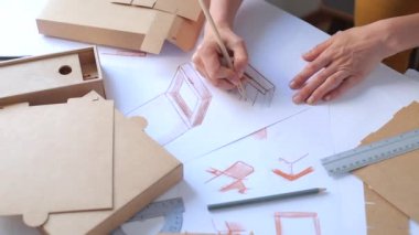  Paketleme tasarımı taslağının geliştirilmesi. Tasarımcı karton kutu yapmak için bir maket çizer. 