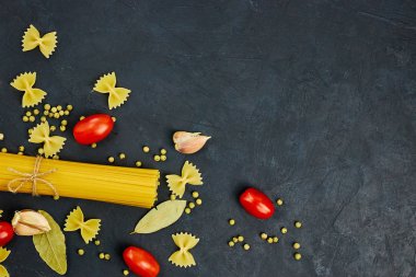 Yemek için çerçeve. Makarna malzemeler. Kiraz domates, spagetti makarna, sarımsak ve baharat bir karanlık grunge arka planda, kopya alanı, görünümü top