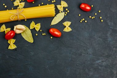 Yemek için çerçeve. Makarna malzemeler. Kiraz domates, spagetti makarna, sarımsak ve baharat bir karanlık grunge arka planda, kopya alanı, görünümü top