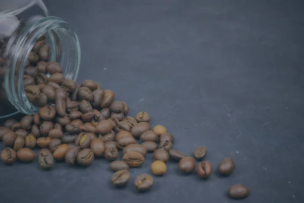 Grains de café torréfiés versés à partir d'un pot en verre. placement angulaire de l'objet café. sur du béton foncé. vue horizontale. espace de copie — Photo