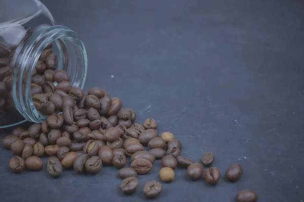 Grãos de café torrados derramados de um frasco de vidro. colocação angular do objeto de café. em betão escuro. vista horizontal. espaço de cópia — Fotografia de Stock