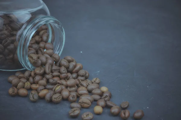 Gebrande koffiebonen gegoten uit een glazen pot. hoekige plaatsing van het koffie-object. op donkere beton. horizontale weergave. kopie ruimte — Stockfoto