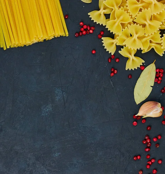 Frame for food. Pasta ingredients. Cherry tomatoes, spaghetti pasta, garlic and spices on a dark grunge background, copy space, top view. Italian pasta.