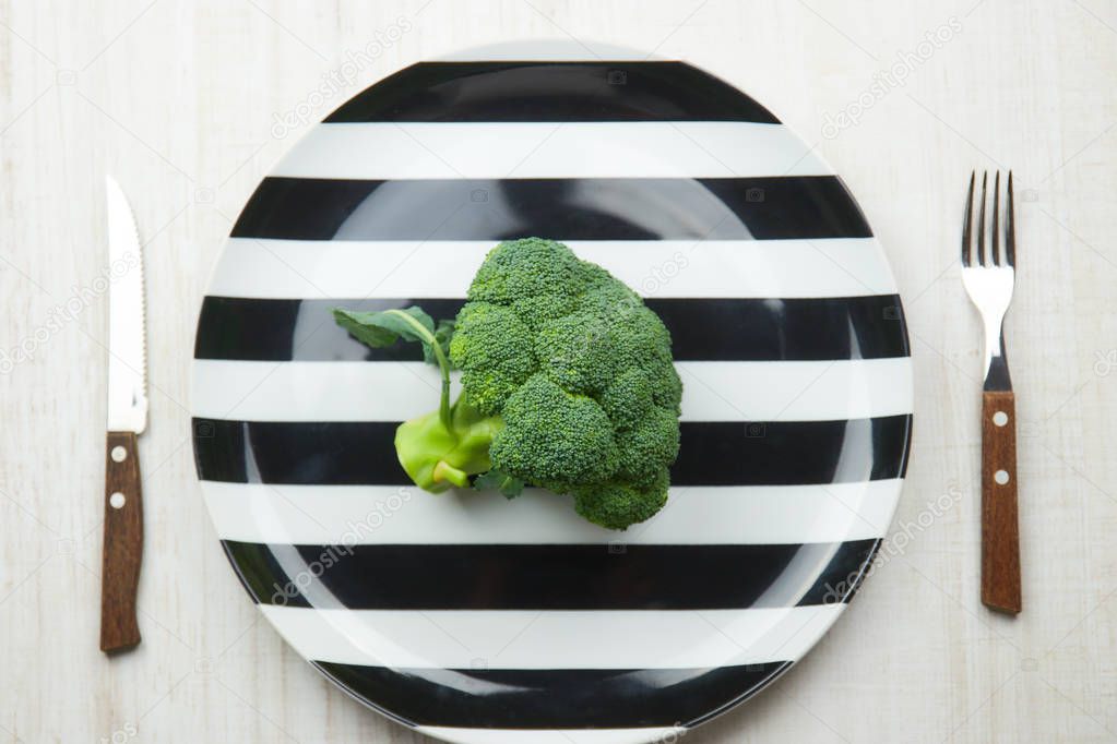 the concept of healthy eating. green, raw broccoli lying on a plate with instruments on a black background. healthy diet. green cabbage close-up. HLS.