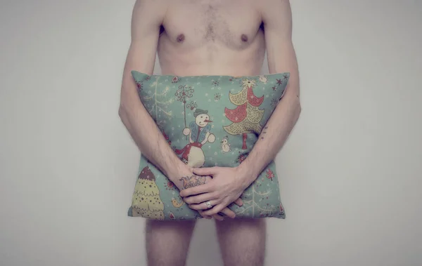 Çıplak genç bir adam onun horoz Noel temalı desenli bir yastık ile kapsar.