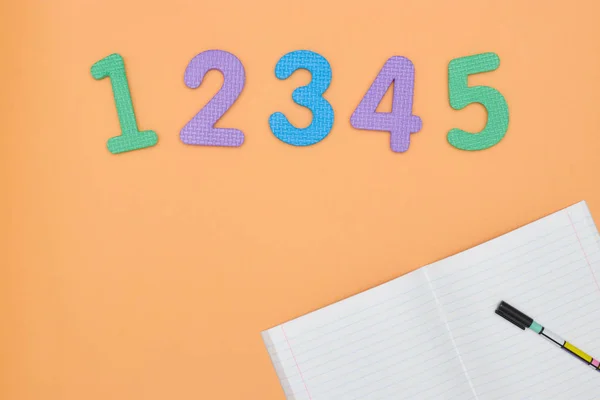 Defter, kalem ve turuncu arka plan üzerinde renkli numaraları. Çalışma için aksesuarlar. Matematik,, düz, kopya alanı