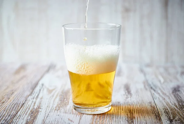 Bir bardak light bira bir ahşap zemin üzerine köpük ile yakın çekim. cam dikey görünüm.