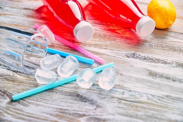 Plastic bottles with berries, refreshing drink. scattered ice cubes and drinking straws. on the background of a shabby wooden table. close up. copy space. — Stock Photo, Image