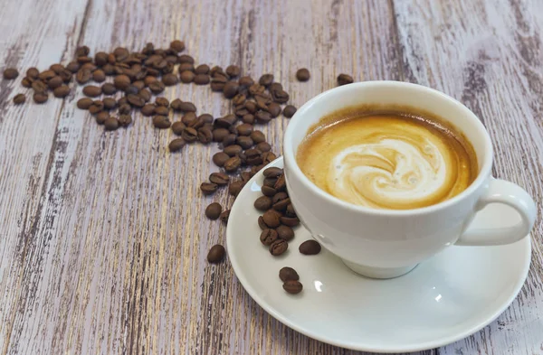 Beyaz fincan sütlü kahve ile. Kahve çekirdekleri ahşap bir masa üzerinde avuç. bir fincan kahve içecek ile yatay görünümünü. Kopya alanı yakın çekim.