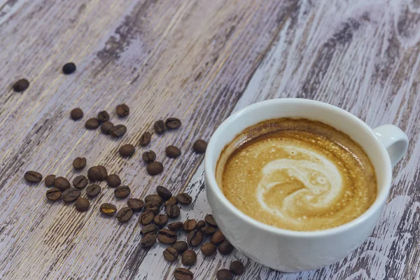 Witte kop met zwarte koffie met melk. Handvol koffiebonen op een houten tafel. horizontale weergave van een kop met een koffie drinken. Kopie ruimte close-up. — Stockfoto