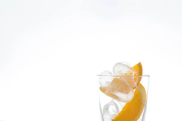Bebida de hielo con naranja y hielo en el estudio sobre un fondo blanco. una corriente de agua vierte en el vaso . —  Fotos de Stock