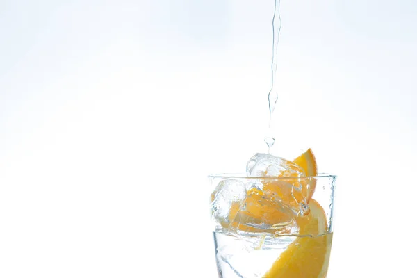 Boisson glacée avec orange et glace dans le studio sur un fond blanc. un jet d'eau se déverse dans le verre . — Photo