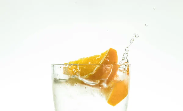 Snijd het oranje segment in een glas water en een spray maken op een witte achtergrond. verneveld water in de lucht. een segment van citrus druppels in een glas spray. — Stockfoto