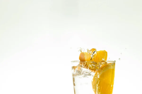 Cortar la rodaja de naranja en un vaso de agua y hacer un aerosol sobre un fondo blanco. spray de agua en el aire. una rebanada de gotas de cítricos en un spray de vidrio . —  Fotos de Stock