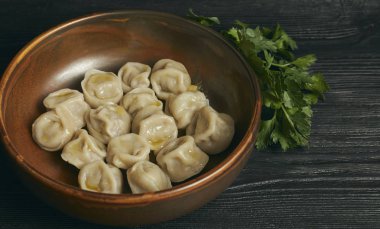 Siyah ahşap masada tereyağı ve yeşillikler ile Pelmeni. Hamur ve kıyma Rus geleneksel yemek. Fotoğraf kapatın. çanak yatay görünümü.