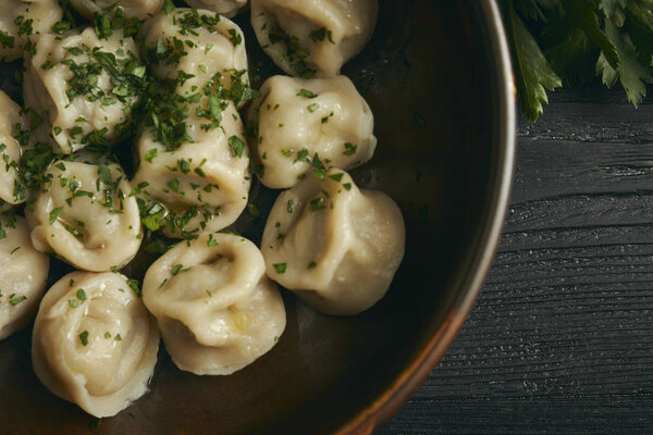 pelmeni with butter and greens on a black wooden table. Russian traditional dish of dough and minced meat. close up photo. horizontal view of the dish.