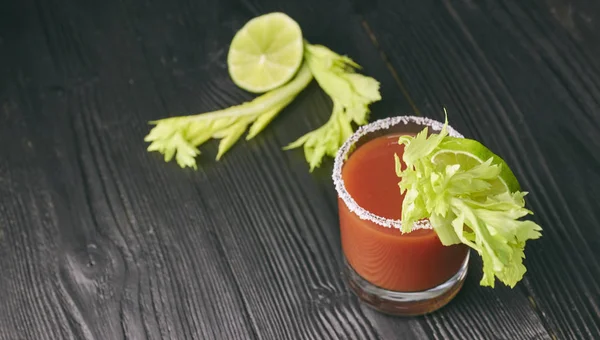 Krwawa mary cockcocktail Bloody Mary z limonką i seler, sól i przekąski w szklance na czarny drewniany stół. poziomy widok cocktail.tail — Zdjęcie stockowe