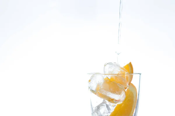 Boisson glacée avec orange et glace dans le studio sur un fond blanc. un jet d'eau se déverse dans le verre . — Photo