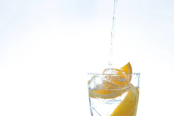 Drankje met oranje ijs en ijs in de studio op een witte achtergrond. een stroom van water giet in het glas. — Stockfoto