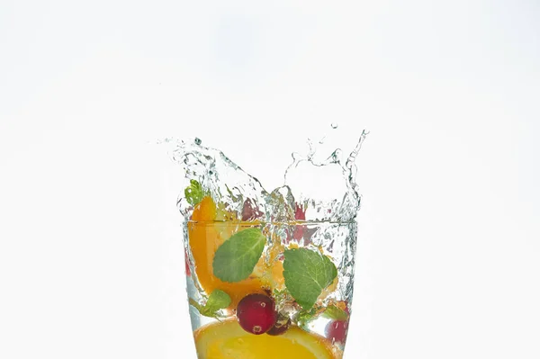 Laranja salpicando em um copo de água com hortelã e bagas em um fundo branco. refrescante bebida de verão com citrinos . — Fotografia de Stock