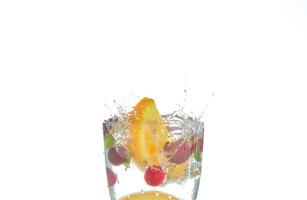 Orange splashing into a glass of water with mint and berry on a white background. minuman musim panas yang menyegarkan dengan jeruk . — Stok Foto