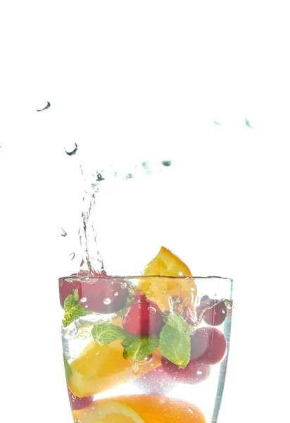 Orange splashing into a glass of water with mint and berry on a white background. minuman musim panas yang menyegarkan dengan jeruk . — Stok Foto