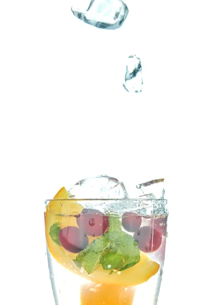 Orange splashing into a glass of water with mint and berry on a white background. minuman musim panas yang menyegarkan dengan jeruk . — Stok Foto