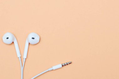 Pastel arka planda kulaklıklar. Şeftali arka planda beyaz kulaklıklar. Yukarıdan bak. Uzayın Moda Renkli Fotoğrafını Kopyala Renkli kağıt arkaplanlı minimal stil. Müzik konsepti