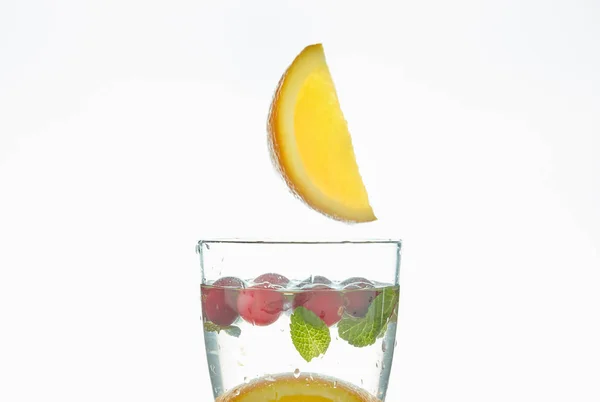 Оранжевый брызг в стакан воды с мятой и ягодами на белом фоне. освежающий летний напиток с цитрусовыми . — стоковое фото