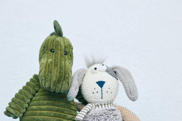 Conejo gris y juguetes de felpa de dinosaurio verde para niños sobre un fondo claro. vista horizontal. Copiar espacio. El concepto de juguetes para niños . — Foto de Stock