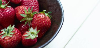 Ahşap beyaz masada bir seramik kase taze kırmızı çilek. taze meyveler. yukarıdan görüntüle. Yazma alanı Kopyala.