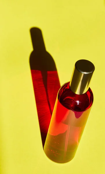 Червона пляшка з тіньовим ефектом ізольована на жовтому фоні. Концепція жіночої косметики та догляду за тілом. Копіювати простір . Стокове Зображення