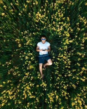 Genç bir adam bir dron çimlerin üzerinden günbatımında başlattı. Renk alanında. Yukarıdan görüntülemek.