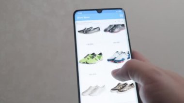 Genç bir adam mobil bir uygulama üzerinden alışveriş yapıyor. İnternetten ayakkabı alıyor. İnternetten alışveriş. Kapatın. Mobil uygulama çevrimiçi mağazası.
