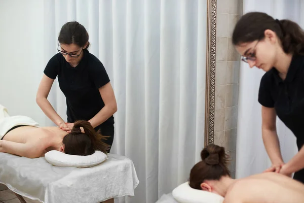 Female therapist massages a young woman on her back and shoulders. Relaxing massage. Therapeutic massage. Alternative medicine. Spa treatments.