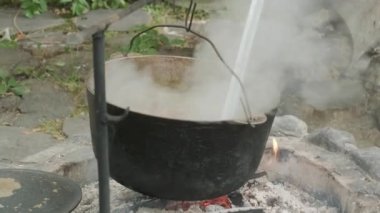 Bir adam, açık ateşte büyük bir kazanda pişirilen büyük bir kaşık mantar çorbasını karıştırır. Doğada yiyecek. Açık hava eğlencesi