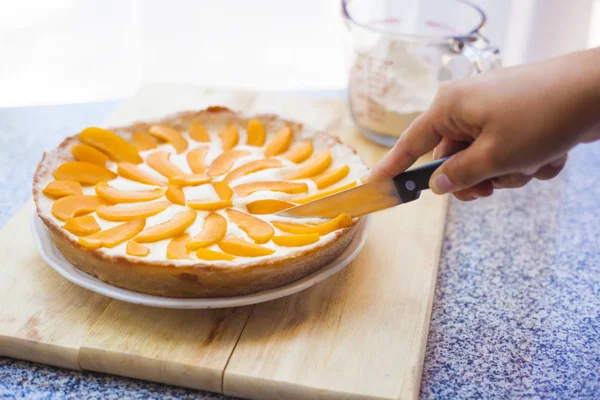 Cutting a piece of tasty homemade lemon apricot pie with a sharp knife on cutting board