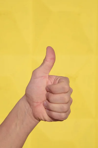 Close-up van mannenhand duimen omhoog teken tegen een gele achtergrond weergeven. — Stockfoto